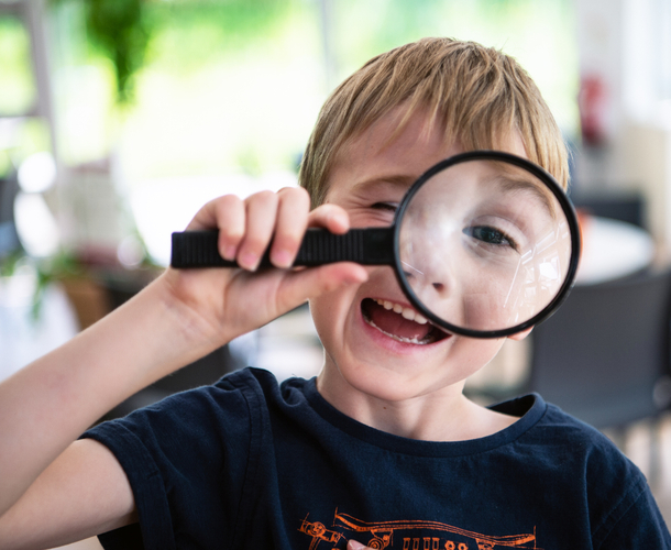 A young boy laughs as he peers through a magnifying glass