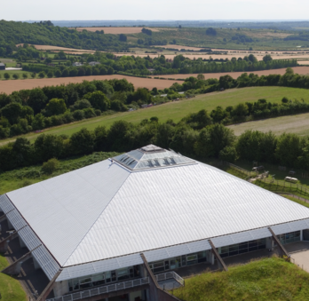 Ariel shot of Winchester Science Centre. The white roof of the iconic pyramid and dome is surrounded by green trees and fields.