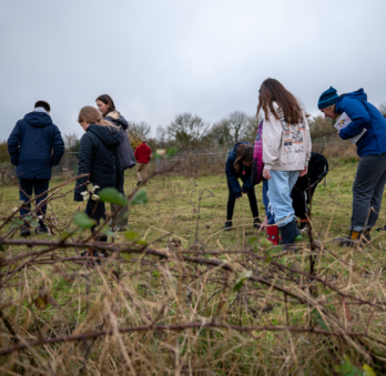 A group of children, wearing thick coats and wellington boots, are exploring the grassland around Winchester Science Centre. They're looking for different types of fungi.