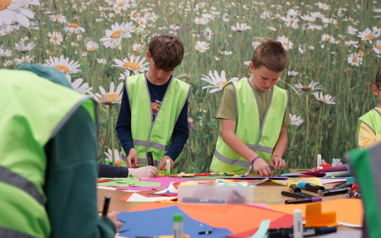 two boys wearing hi-vis jackets are create a collage of the different shapes found in  the Science Centre's natural landscape