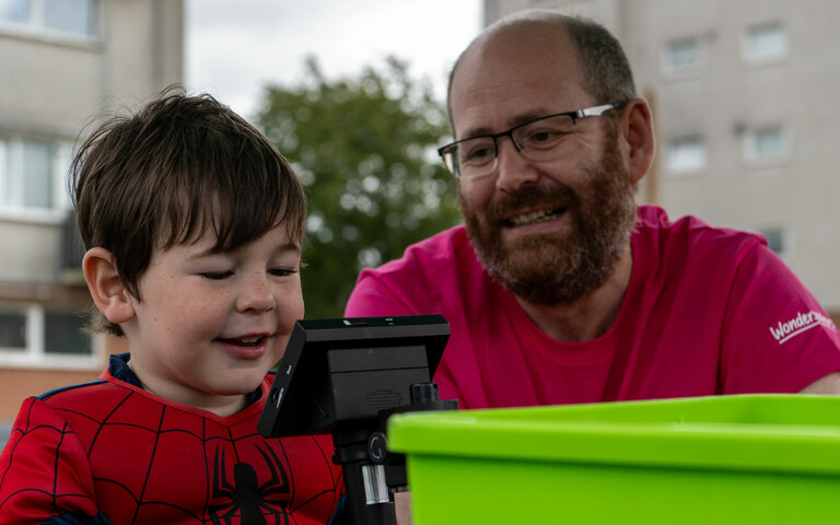 A child looks at a microscope with an adults support