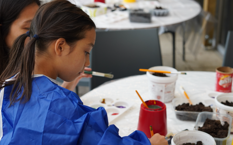 Girl in a blue apron is painting a small plant pot