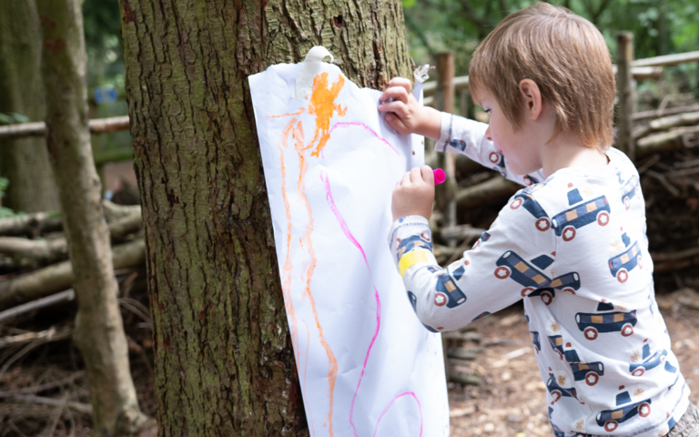 Child colouring leaning up against a tree as part of mark making.