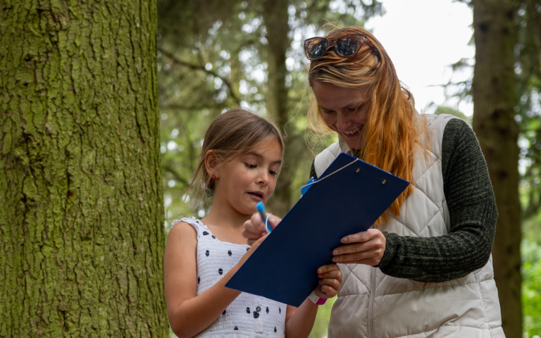 Mother and child stood by a tree looking at a clipboard.