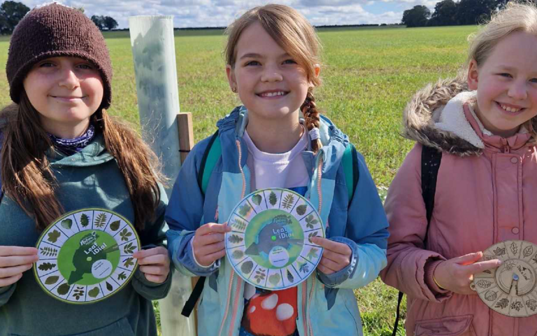 Three children are smiling and holding paper leaf dials.