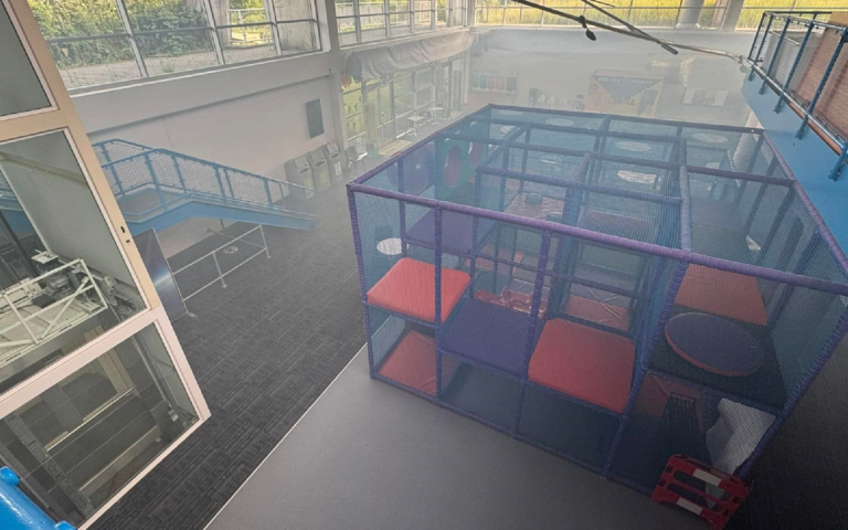 The exhibition floor with a small soft play structure is filled with smoke. The room looks misty.