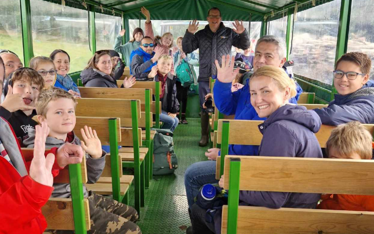 The Young Design Panel are sat in a trailer attached to a tracker. The children are smiling and waving.